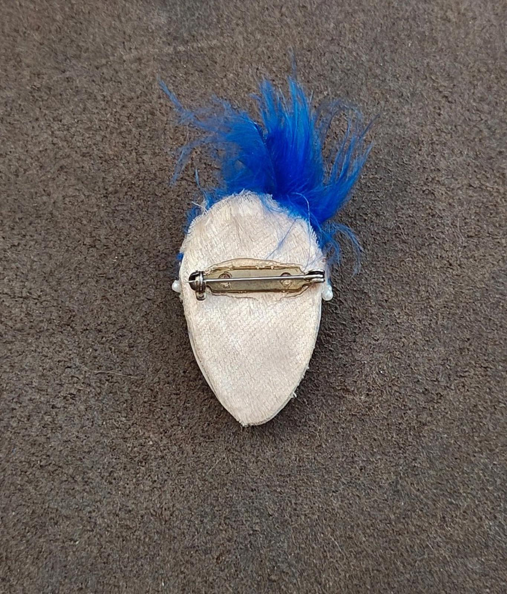 Back of doll face pin brooch with blue feather and gold-tone pin clasp