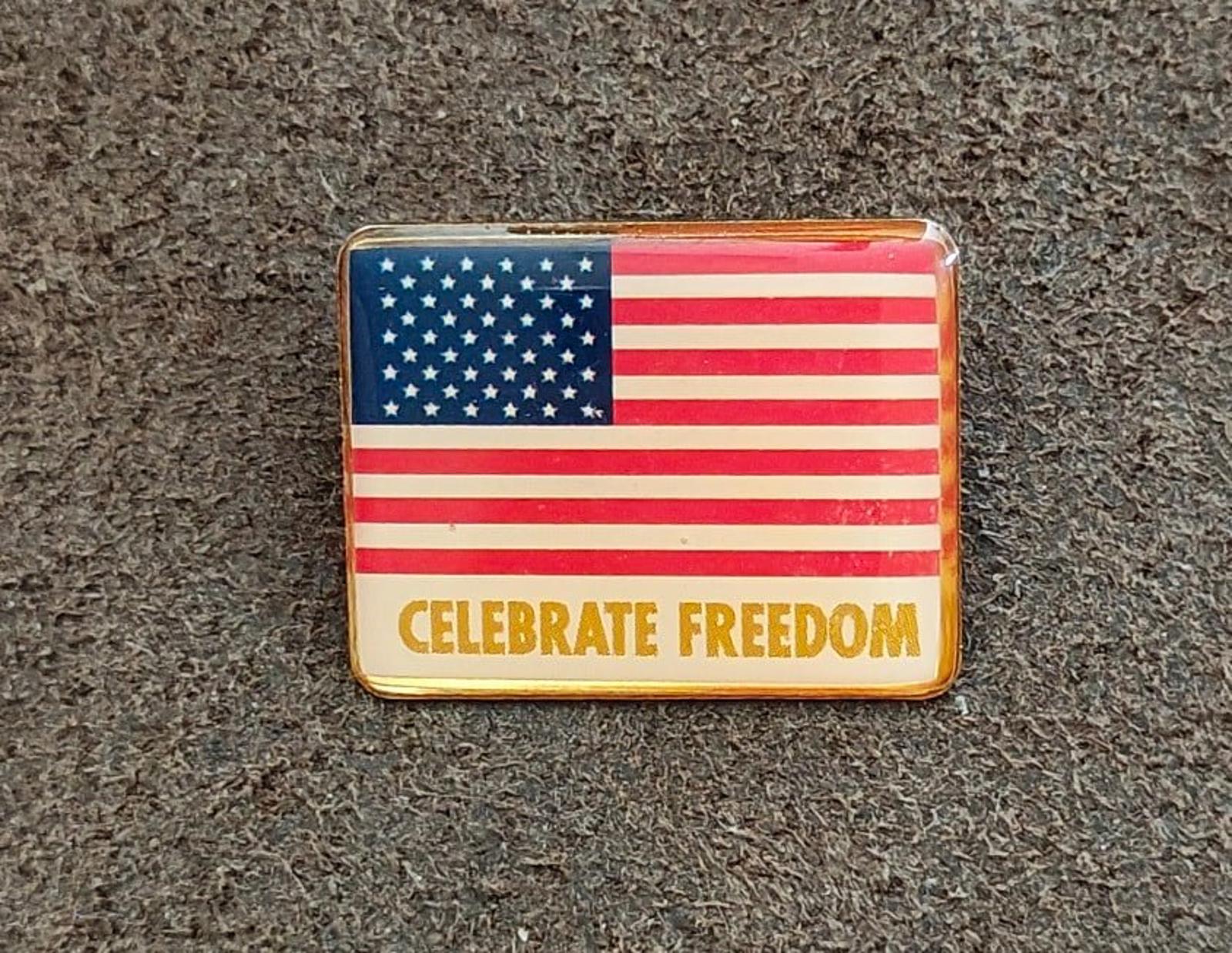Gold-tone American flag pin with “CELEBRATE FREEDOM” lettering across the bottom