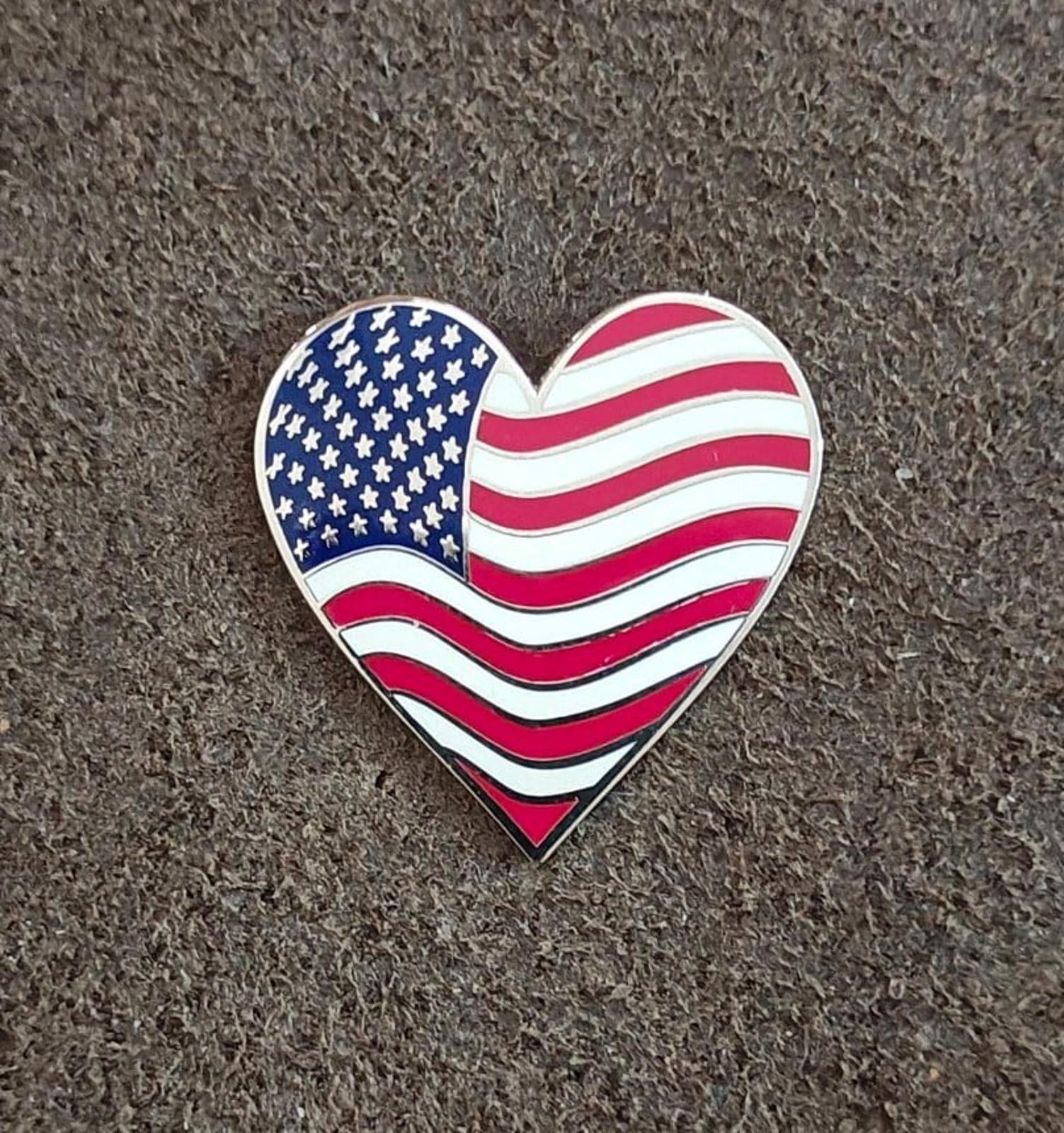 Heart-shaped American flag enamel pin with wavy red and white stripes over blue stars
