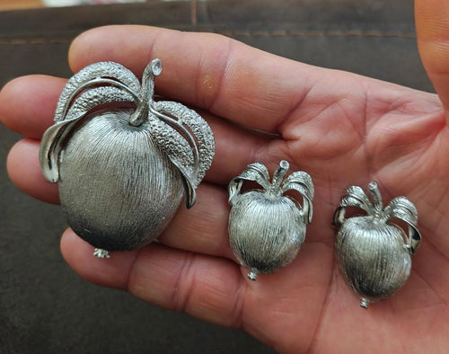 Silver-tone apple brooch with leaf details, plus two matching apple earrings on display