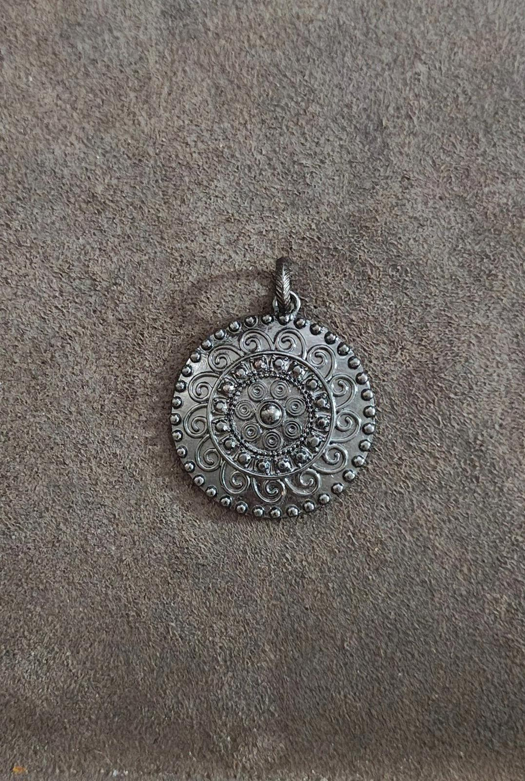 Round gunmetal pendant with embossed floral scroll pattern and stone-like center