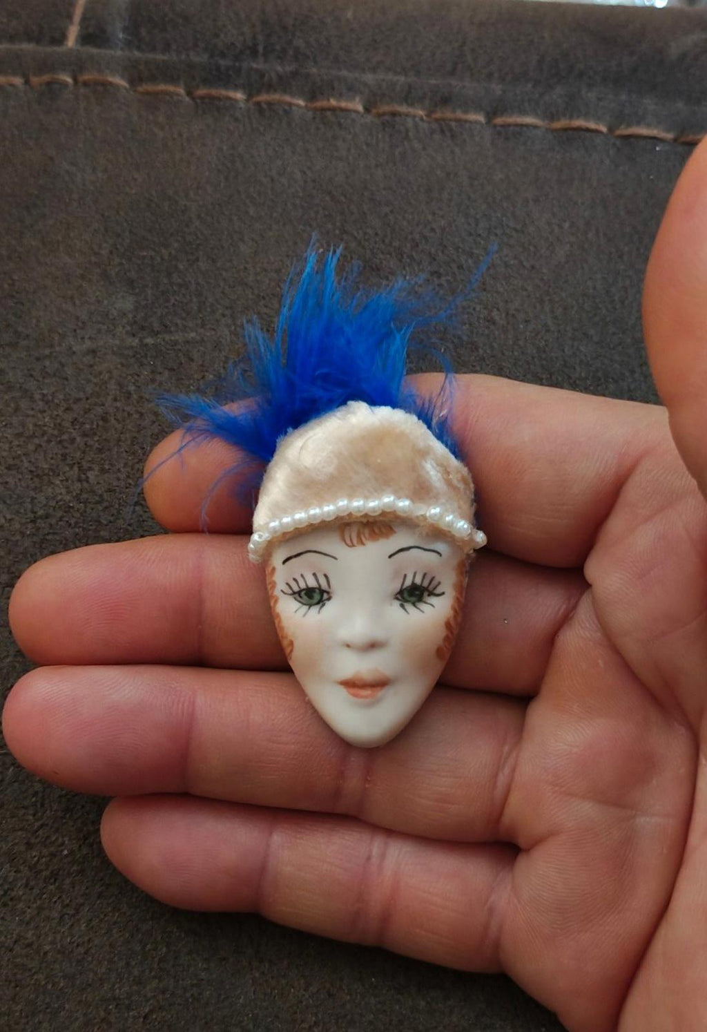 Doll face pin brooch with blue feather plume and cream pearl-trim headband