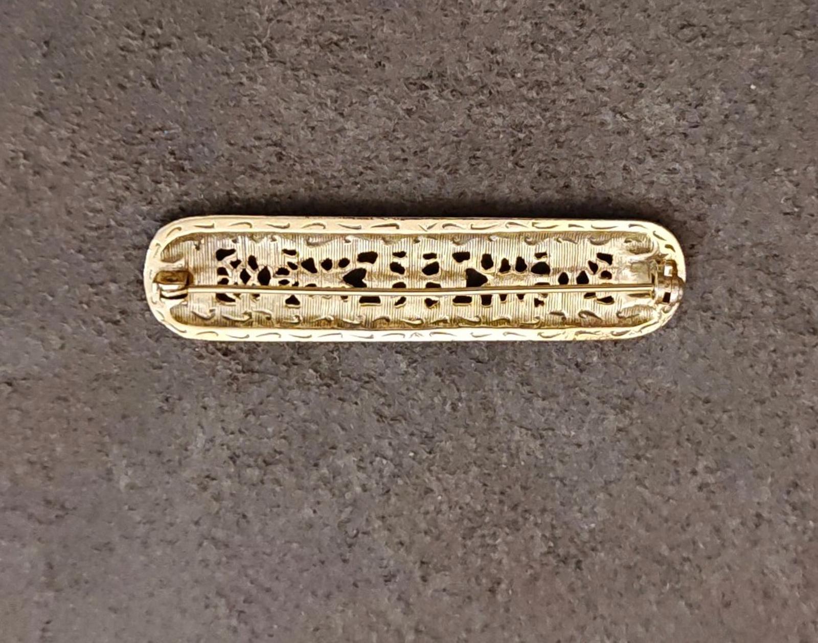 Gold tone oval bar brooch featuring detailed filigree latticework along the frame.