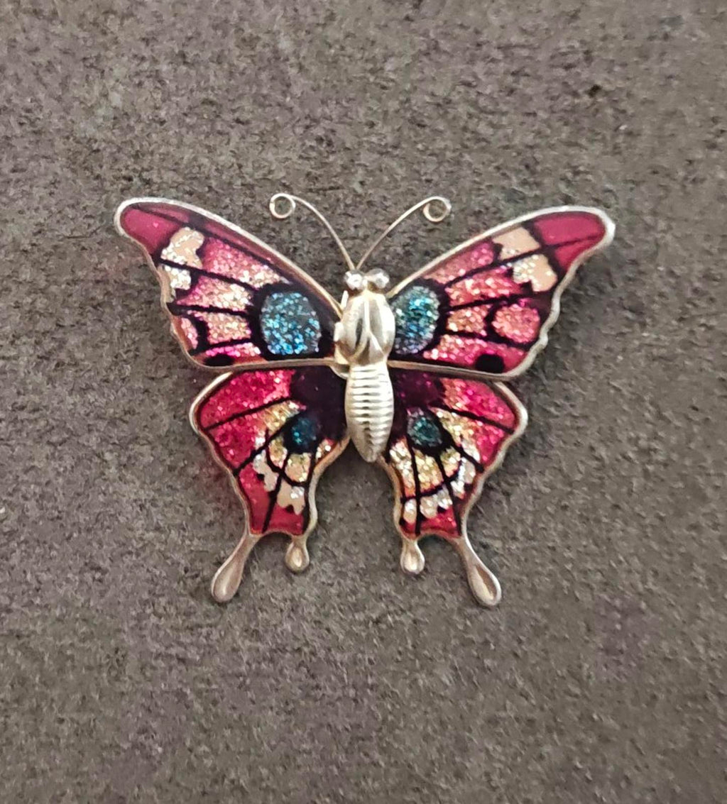 Butterfly enamel brooch on dark surface, red wings with blue glitter and gold-tone details