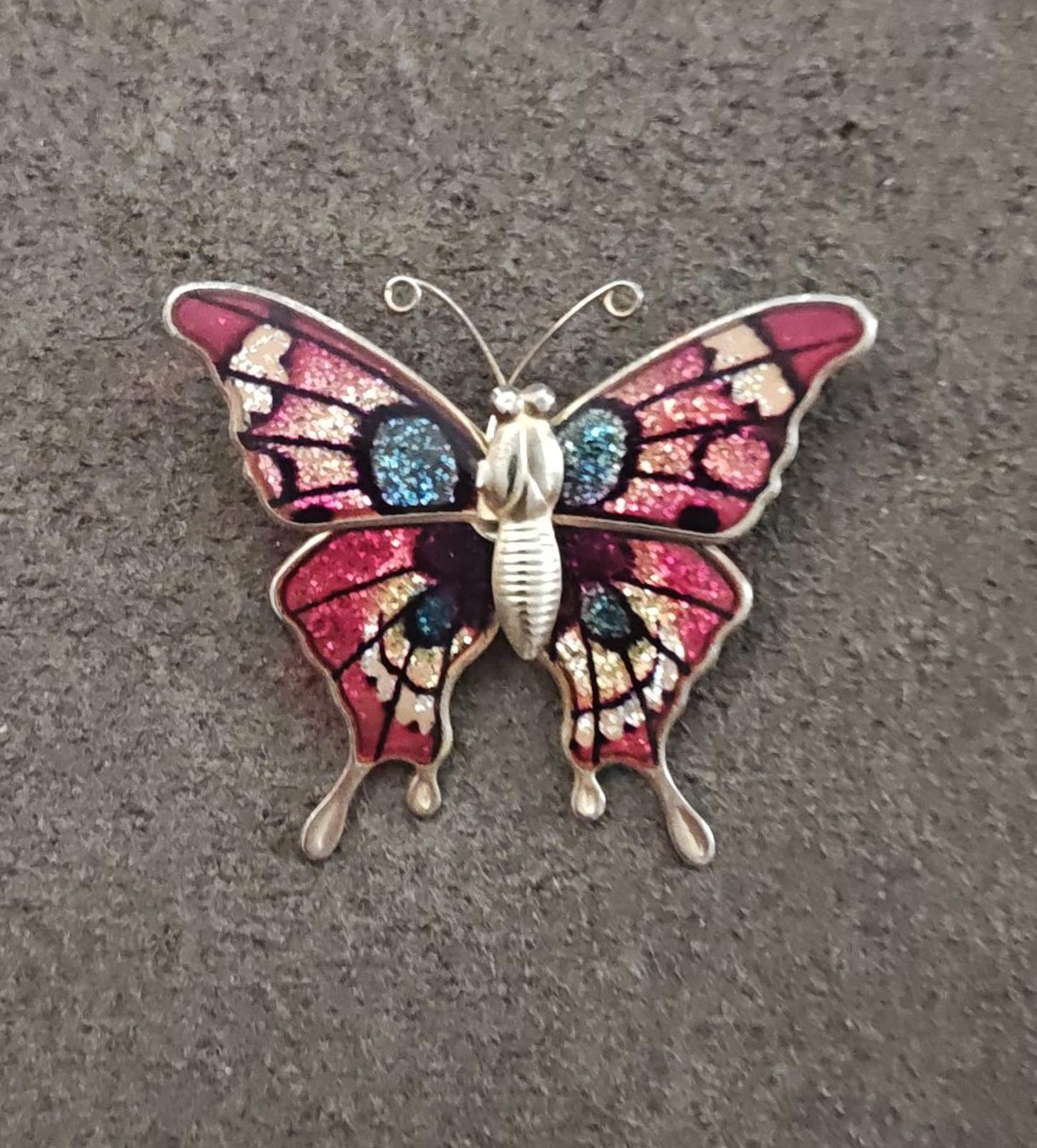 Butterfly enamel brooch on dark surface, red wings with blue glitter and gold-tone details