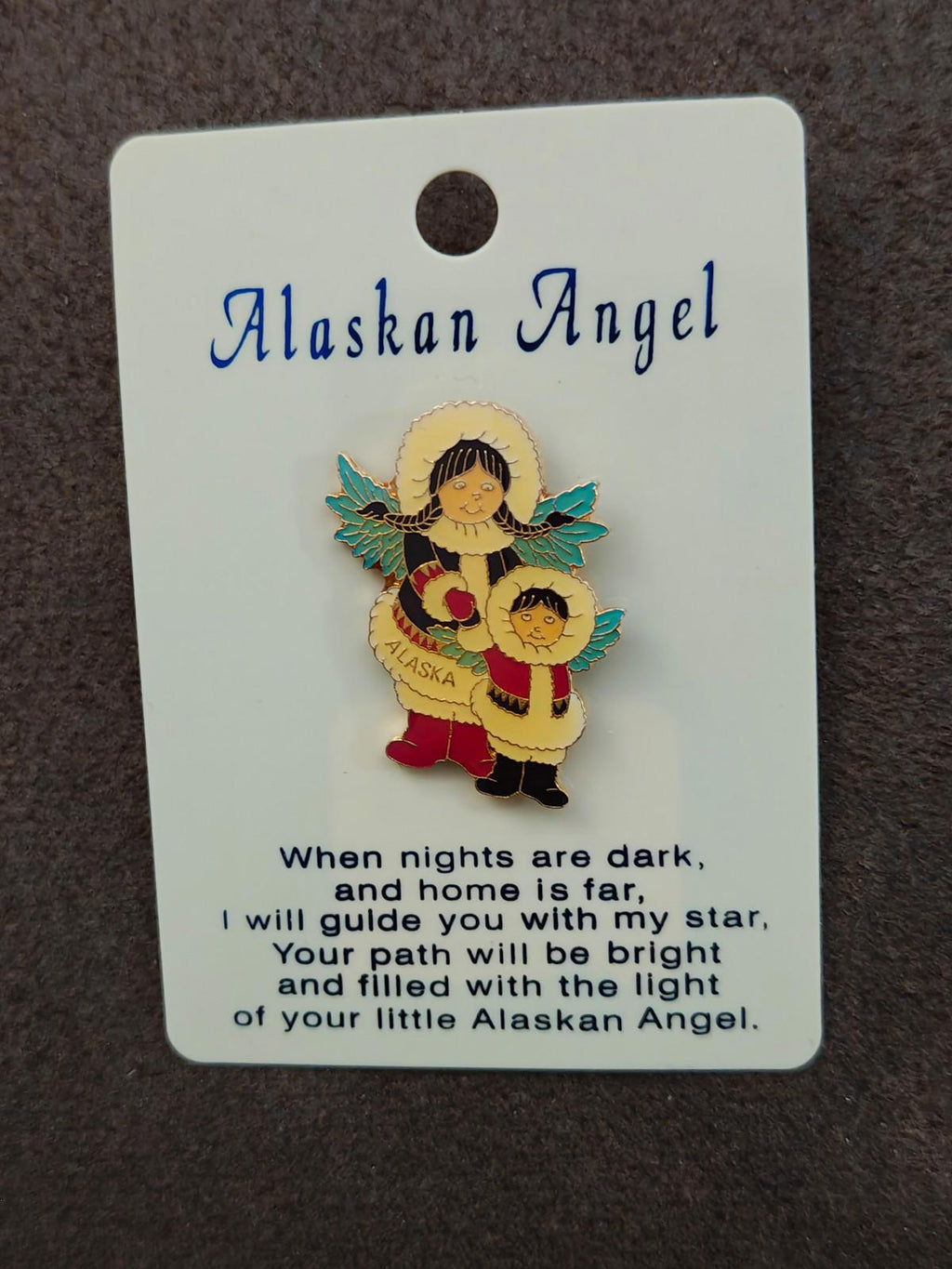 Angel enamel pin with wings and child figure, displayed on a card