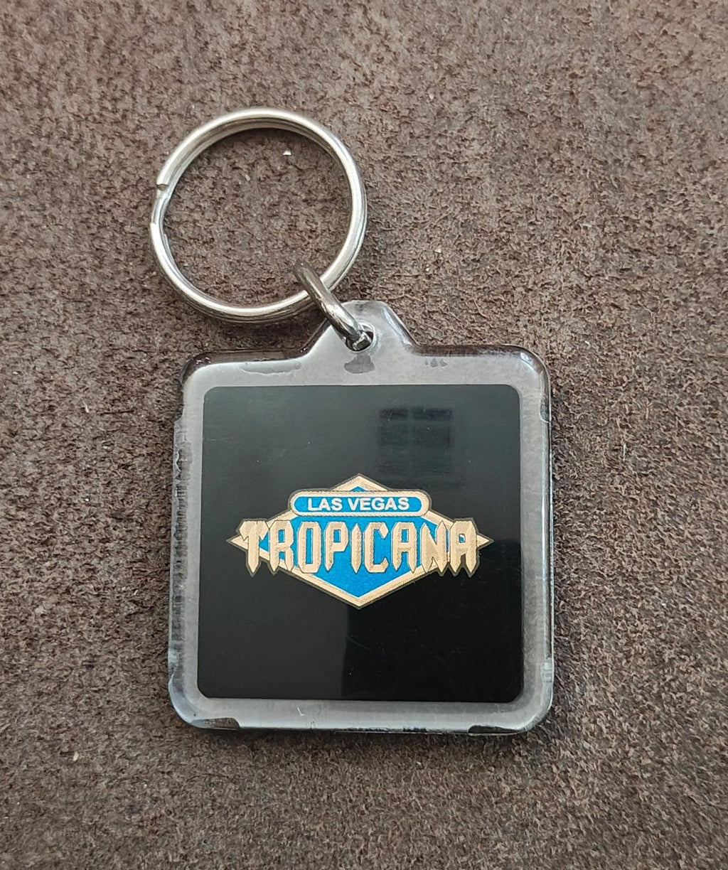 Square Tropicana logo keychain badge with silver ring on speckled carpet