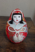 Red and silver Japanese Hime Daruma doll with painted face, long black hair, tassel trim