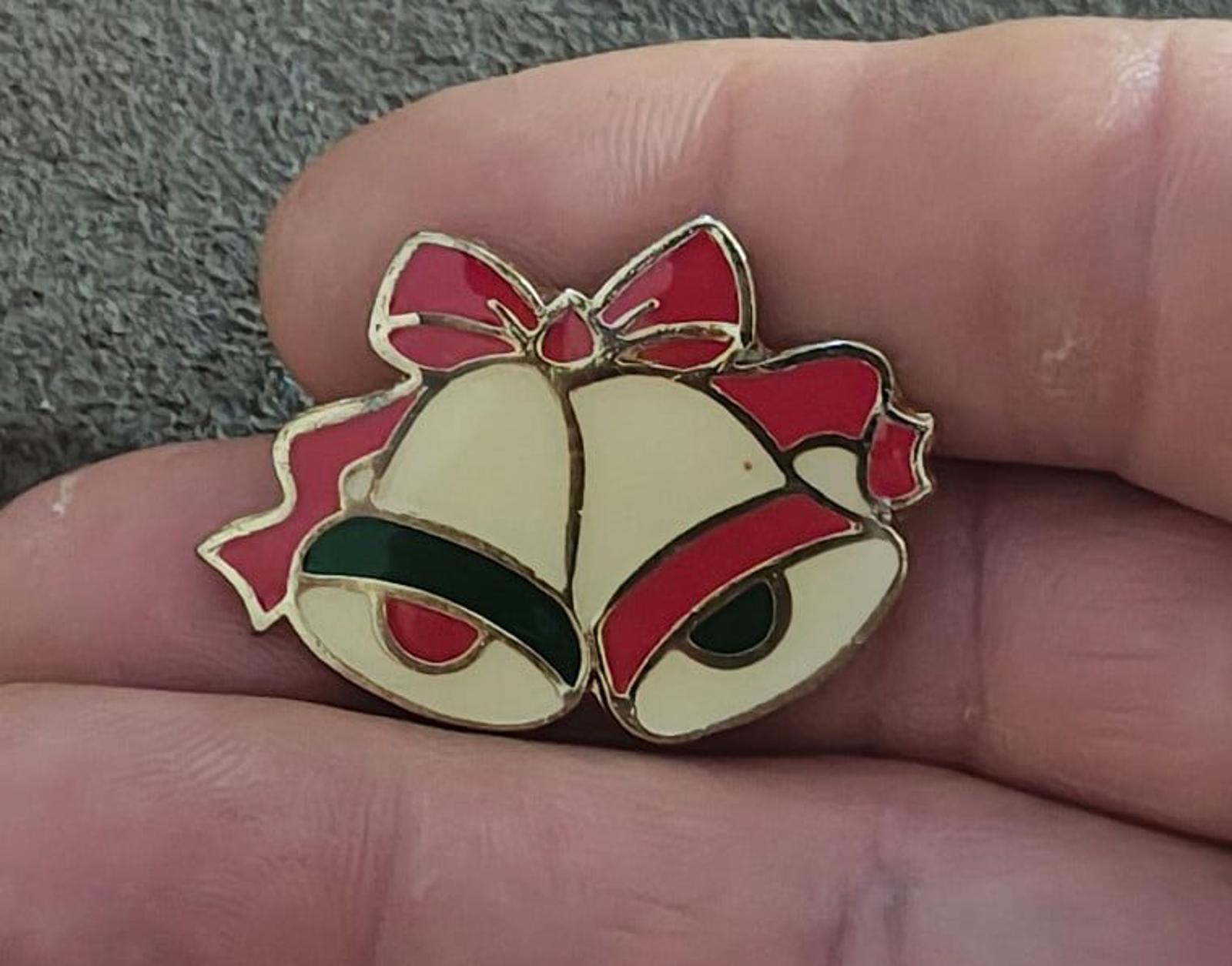 Gold tone enamel Christmas bells brooch with red bow accents and green clappers, hand-held close-up