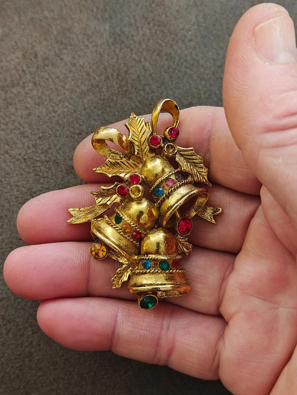 Gold tone Christmas bell brooch with red, green, and blue rhinestones, held in hand