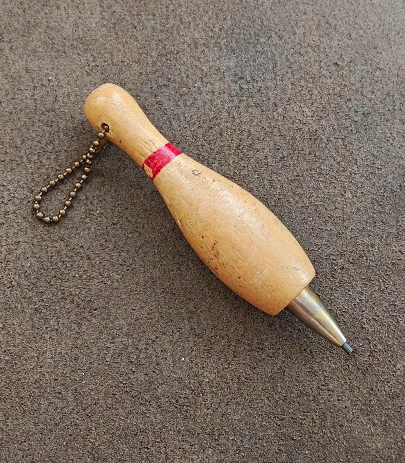 Beige wooden bowling pin mechanical pencil keychain on its side with red band and chain