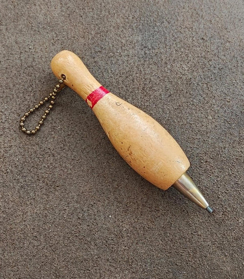 Beige wooden bowling pin mechanical pencil keychain on its side with red band and chain