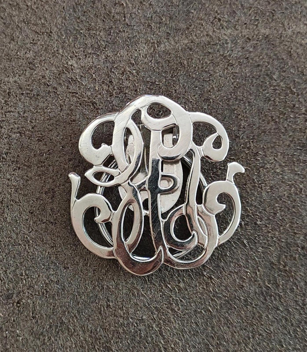 Silver-tone monogram scarf clip, close-up of polished ornate monogram