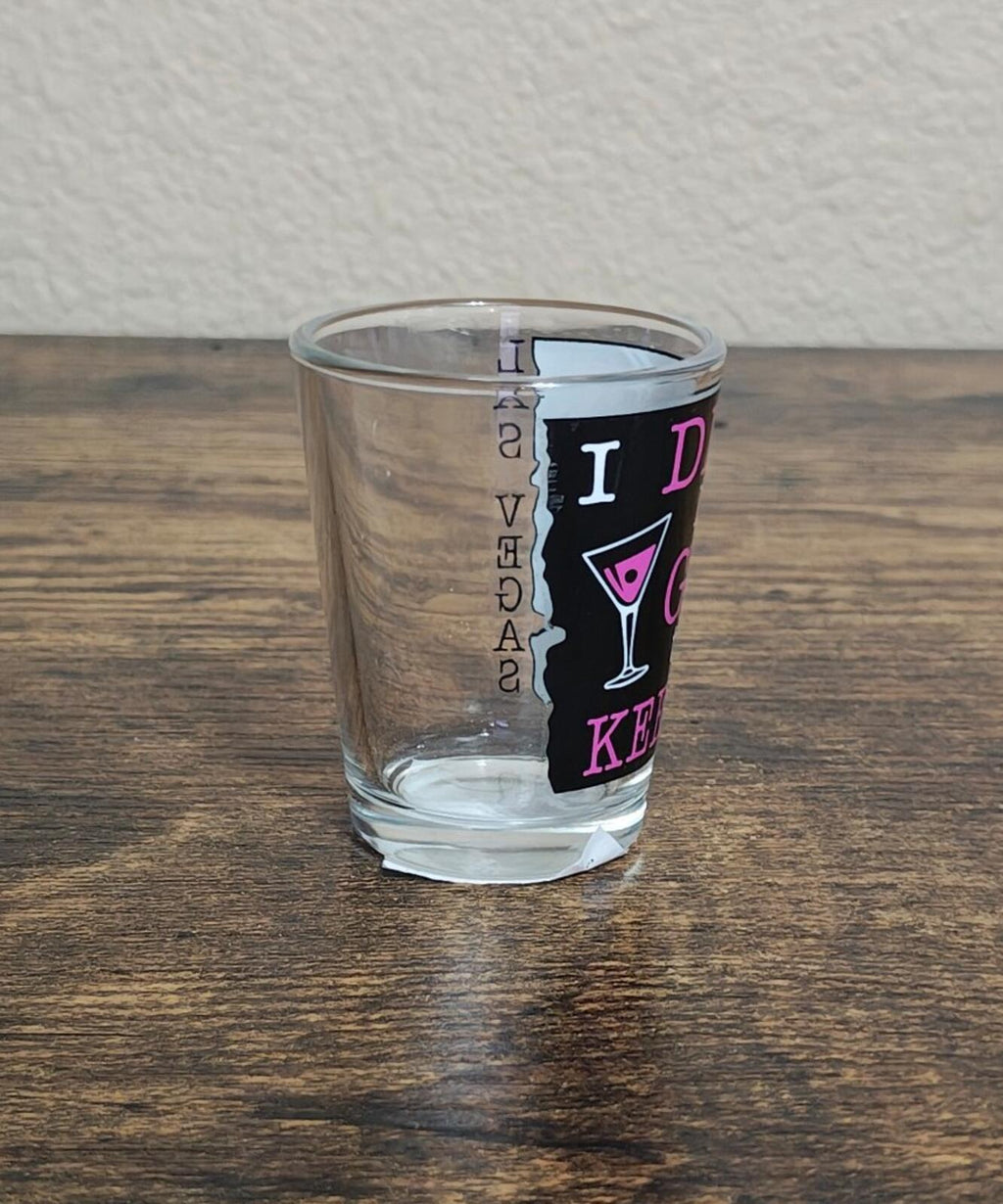 Clear shot glass with martini icon and purple/pink “DRINK” text, angled view