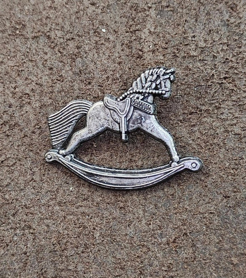 Silver-toned pewter rocking horse pin on the surface, side profile with curved rockers.