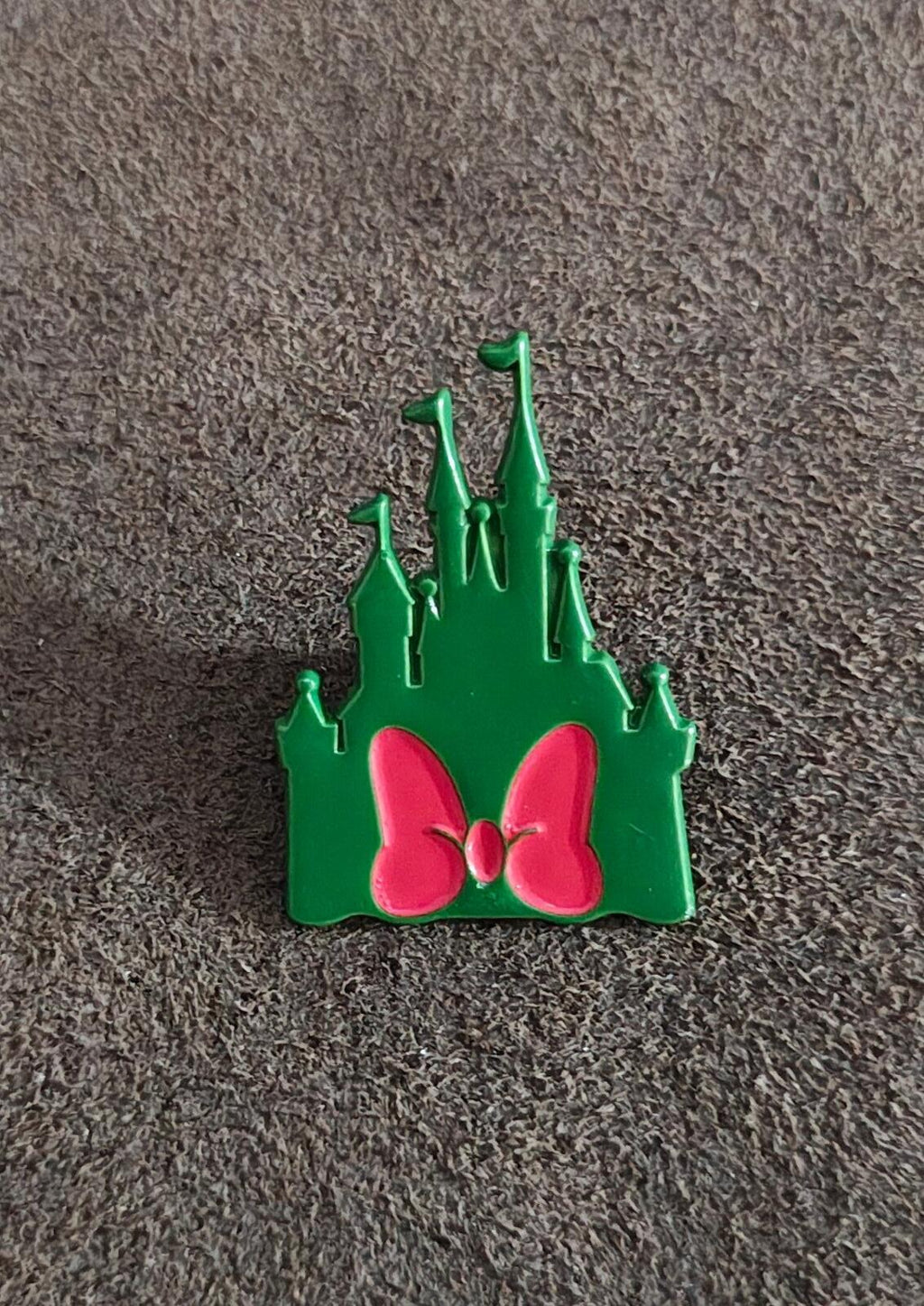 Green castle enamel pin with pink bow and raised spires on textured surface