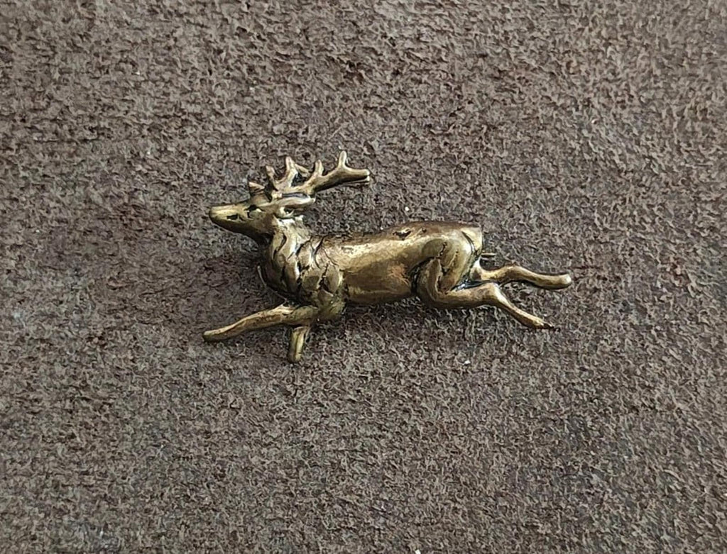 Brass deer figurine in running stance on textured gray surface, wide view