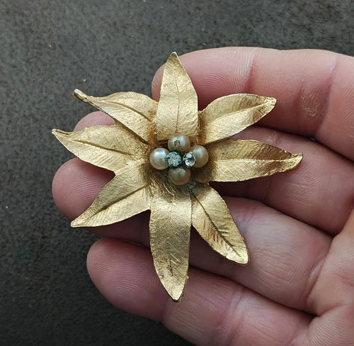 Gold tone textured flower brooch with faux pearls and rhinestone center, held in hand