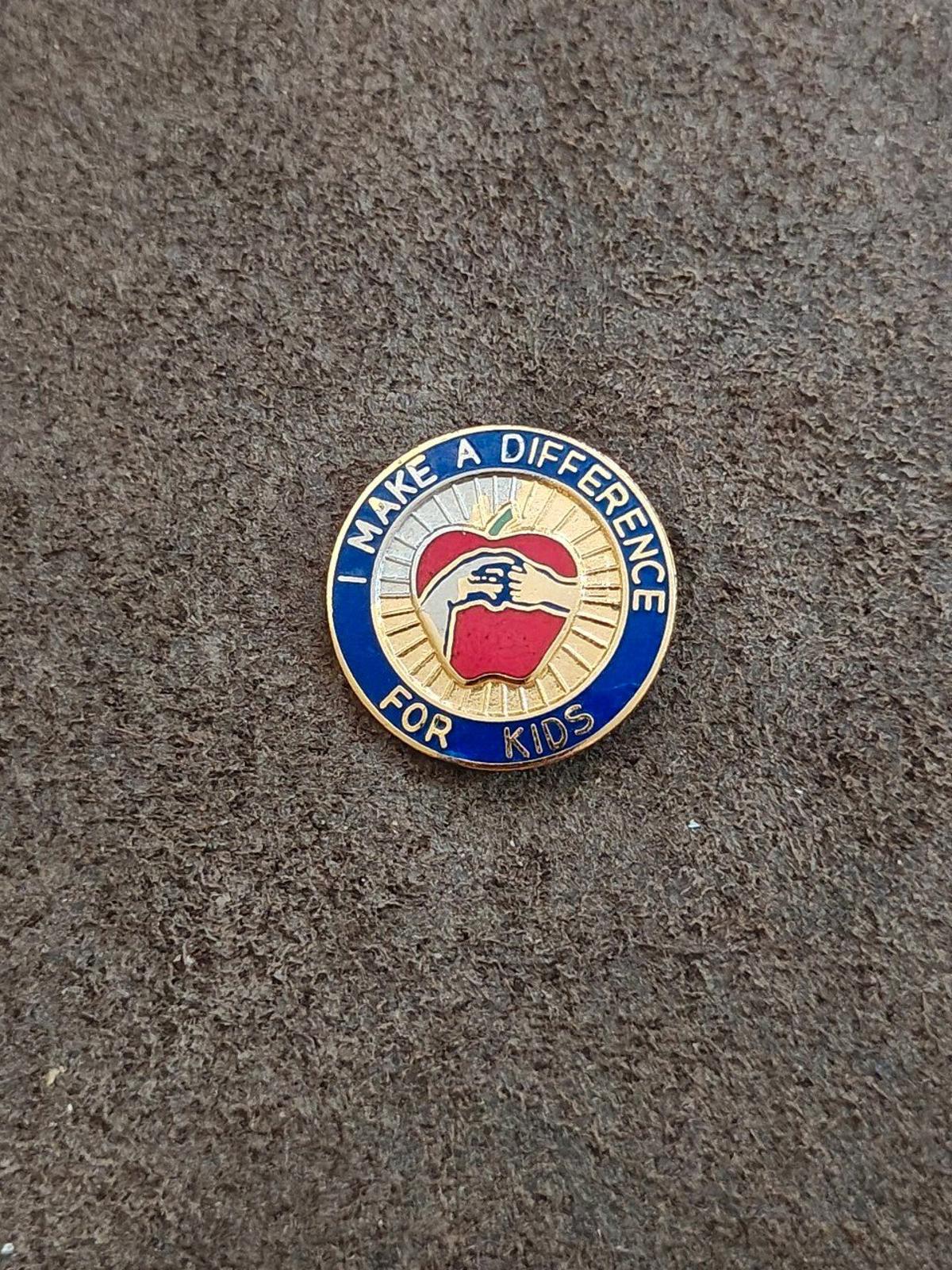 Round blue-and-gold enamel “Make a Difference for Kids” pin, apple graphic centered.