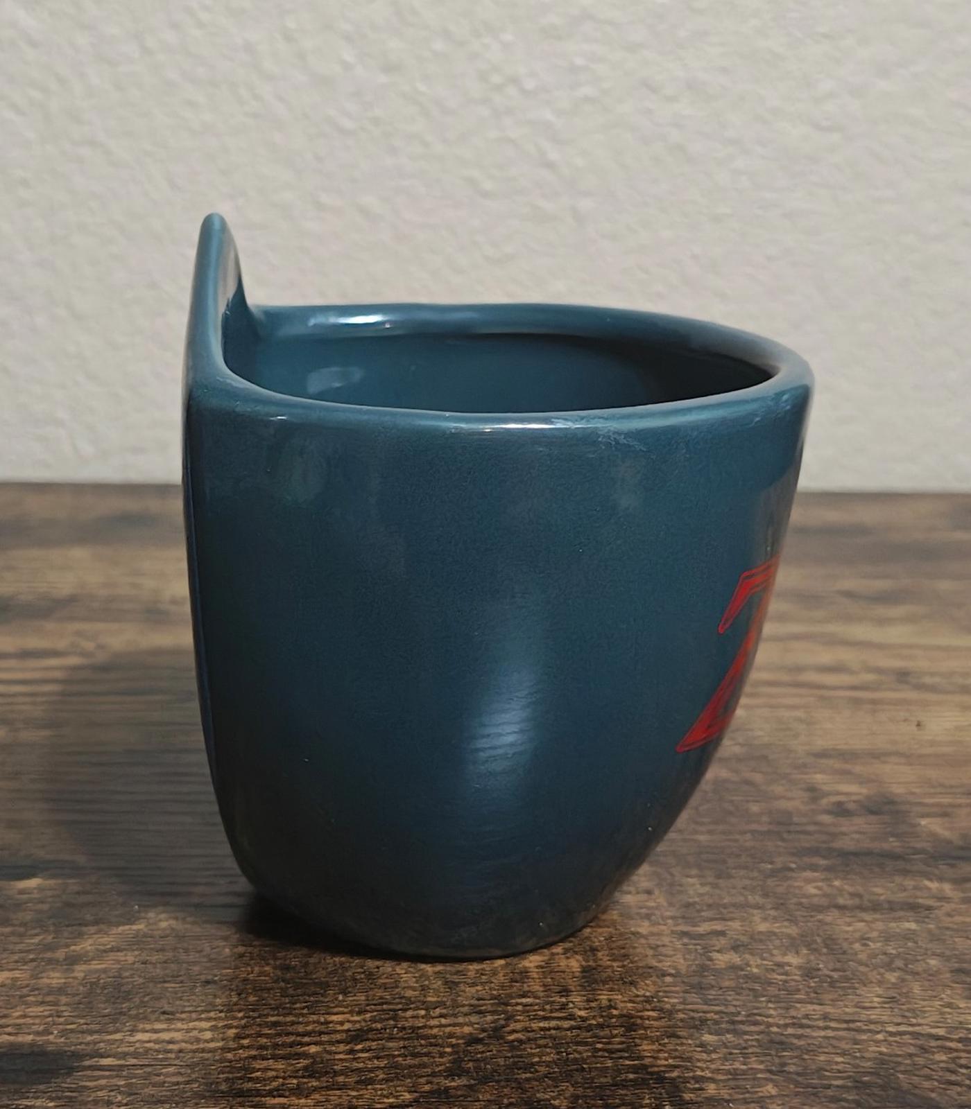 Blue mug with partial shield mark on the back, side view.