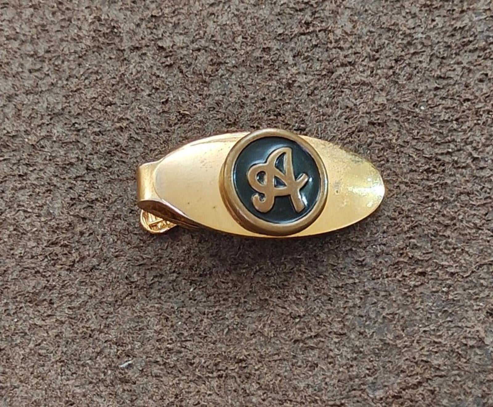 Gold-tone tie clip with oval body and blue-black round monogram emblem
