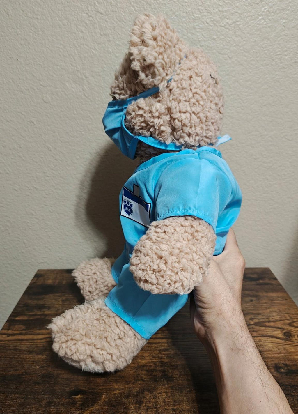 Brown teddy bear plush in blue scrubs, side view with hood and back badge patch