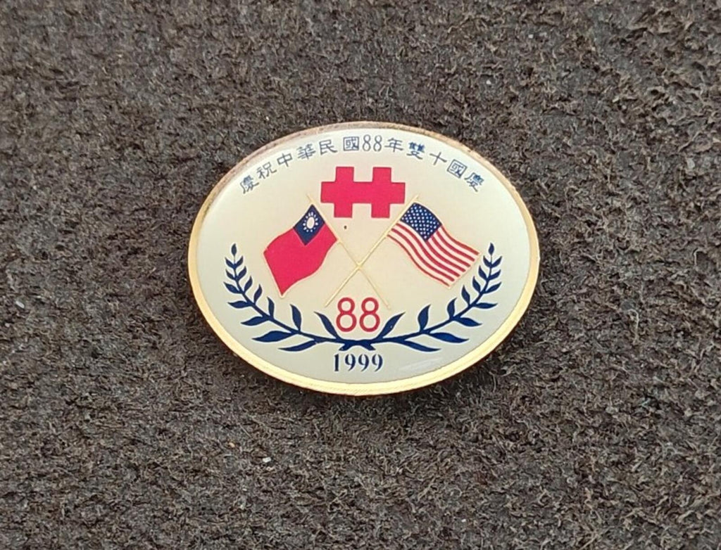 Round gold enamel national day pin showing flags, 88 and 1999, laurel wreath