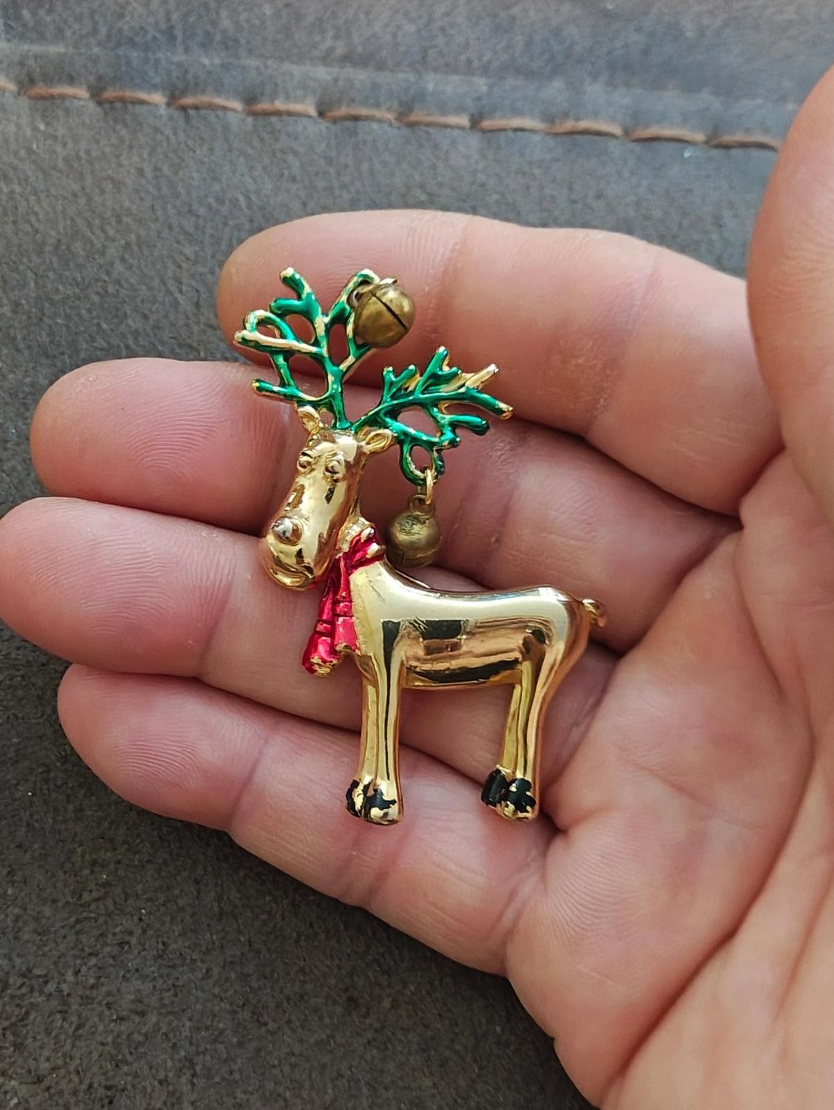 Gold-tone reindeer pin brooch, close-up in hand, green antlers and red scarf.