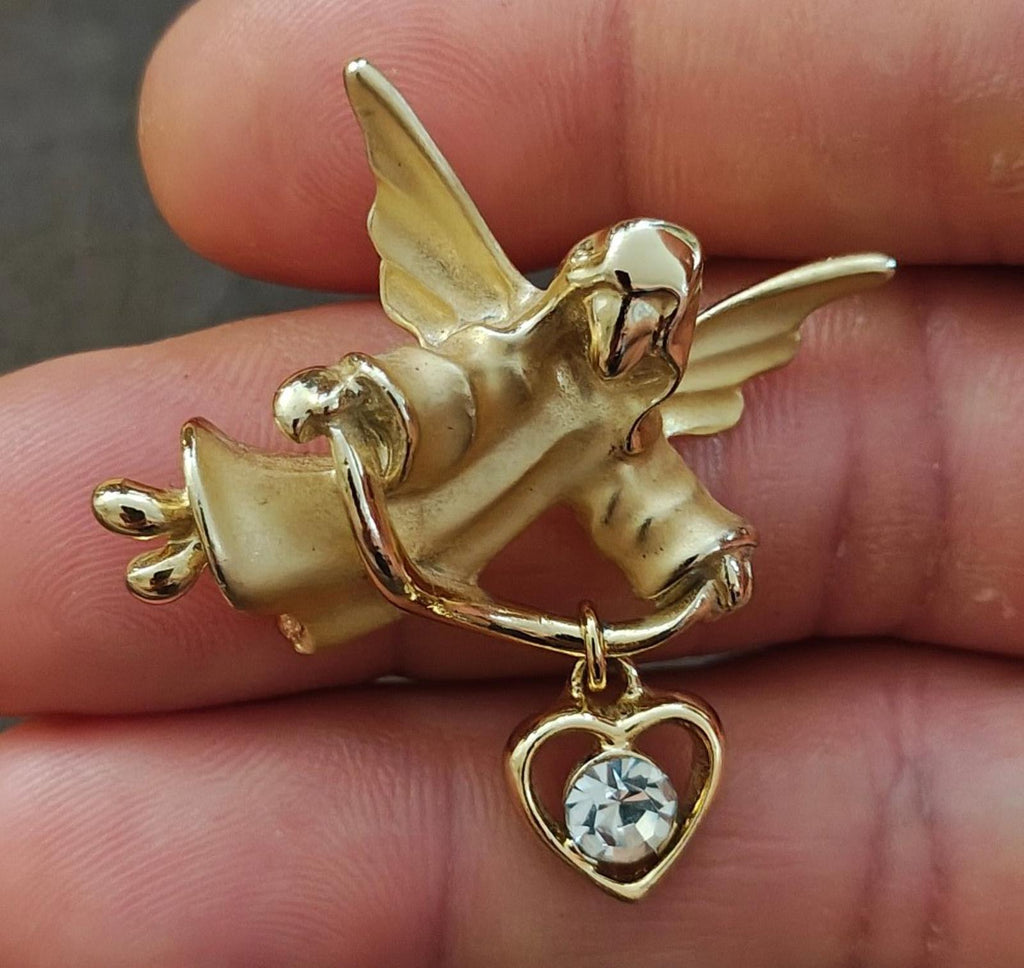 Gold-tone angel brooch pin holding a heart charm with a crystal-like stone