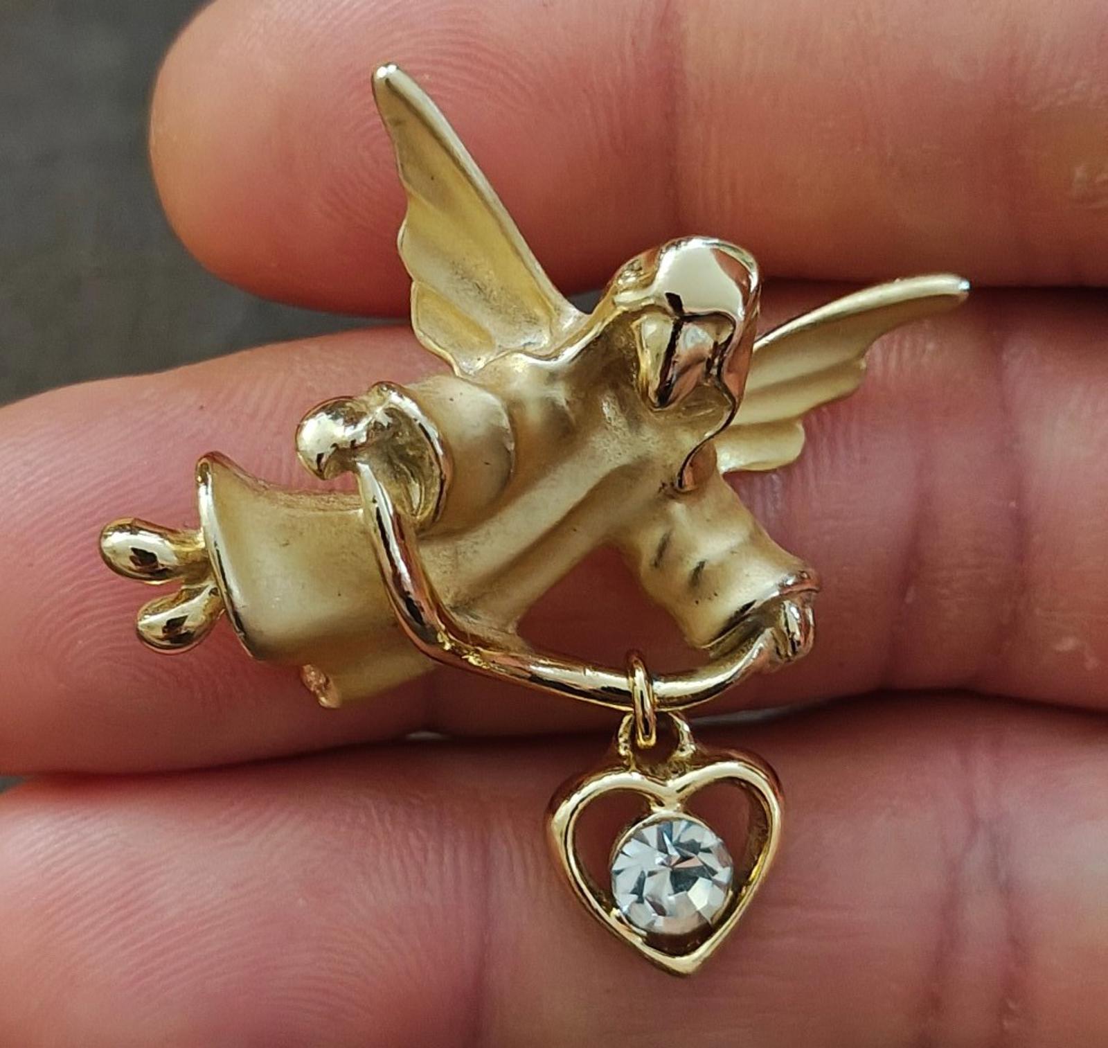 Gold-tone angel brooch pin holding a heart charm with a crystal-like stone