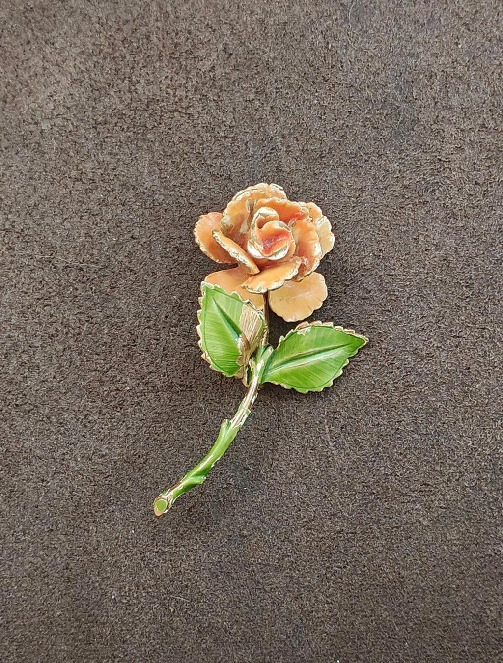 Gold-tone enamel rose pin with orange petals and green leaves, shown against dark surface