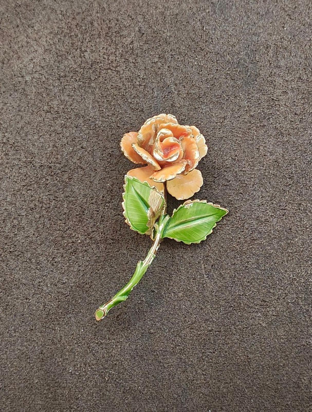Gold-tone enamel rose pin with orange petals and green leaves, shown against dark surface