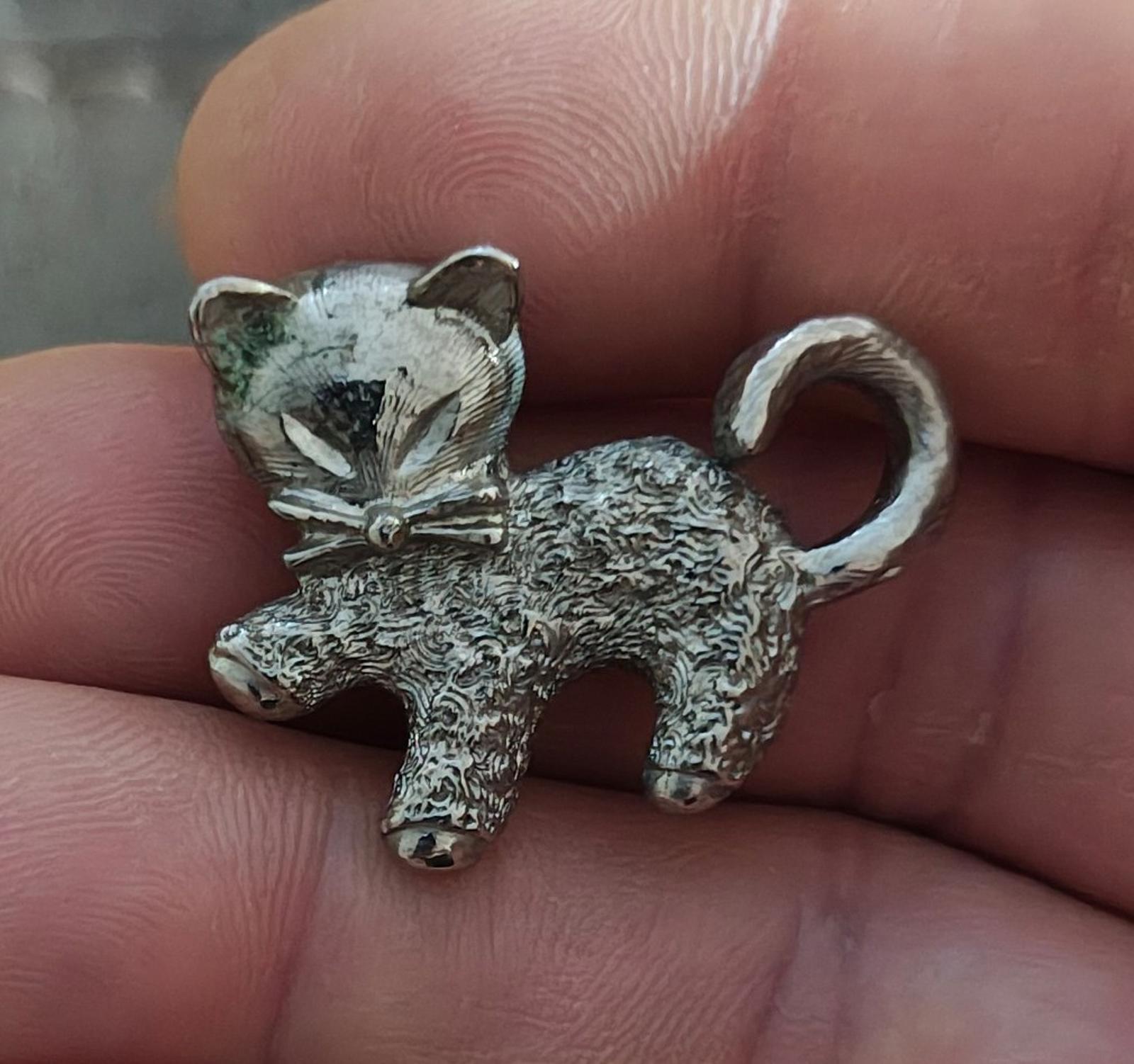 Silver-tone textured cat brooch pin in hand, bow detail and curled tail.