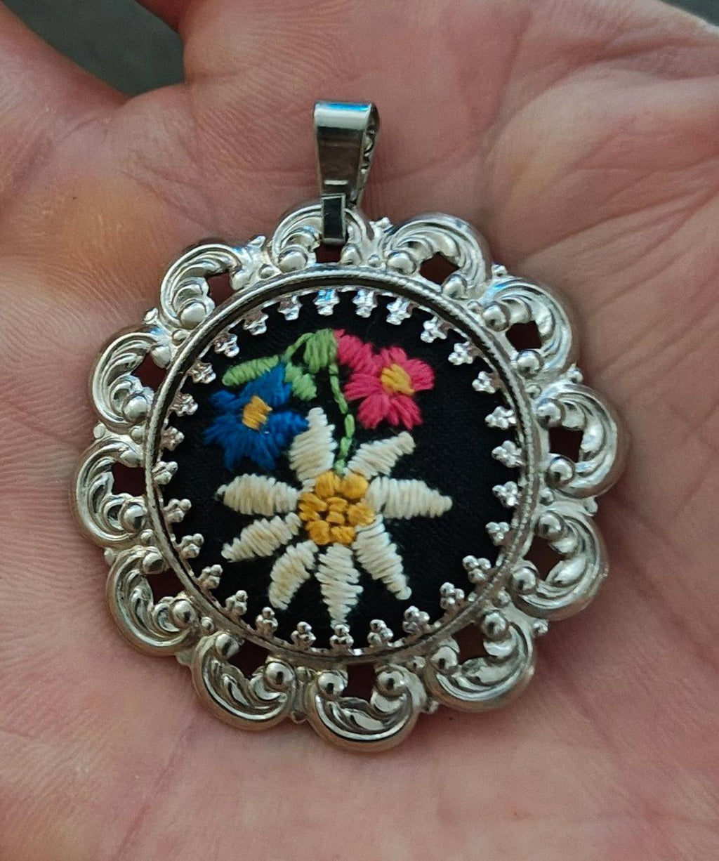 Silver filigree pendant with round black floral embroidery and a top bail loop.