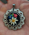 Silver filigree pendant with round black floral embroidery and a top bail loop.
