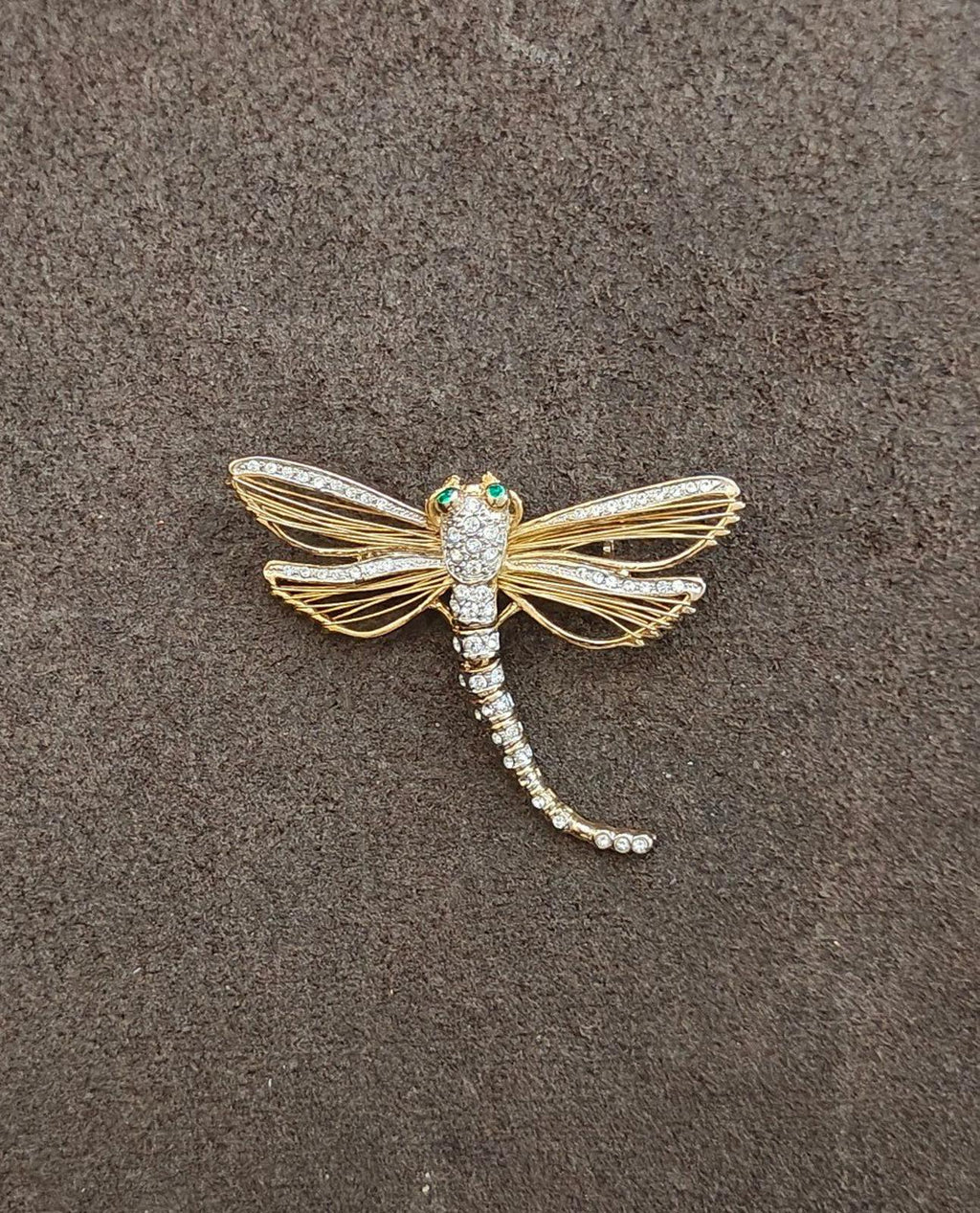 Gold-tone dragonfly rhinestone pin with green enamel eyes, full view on dark surface