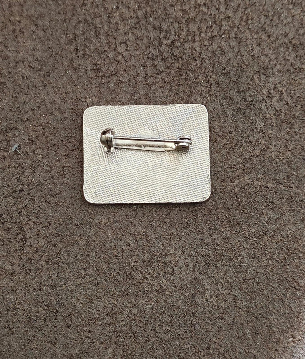 Metal lapel pin clasp on white backing card, silver tone.