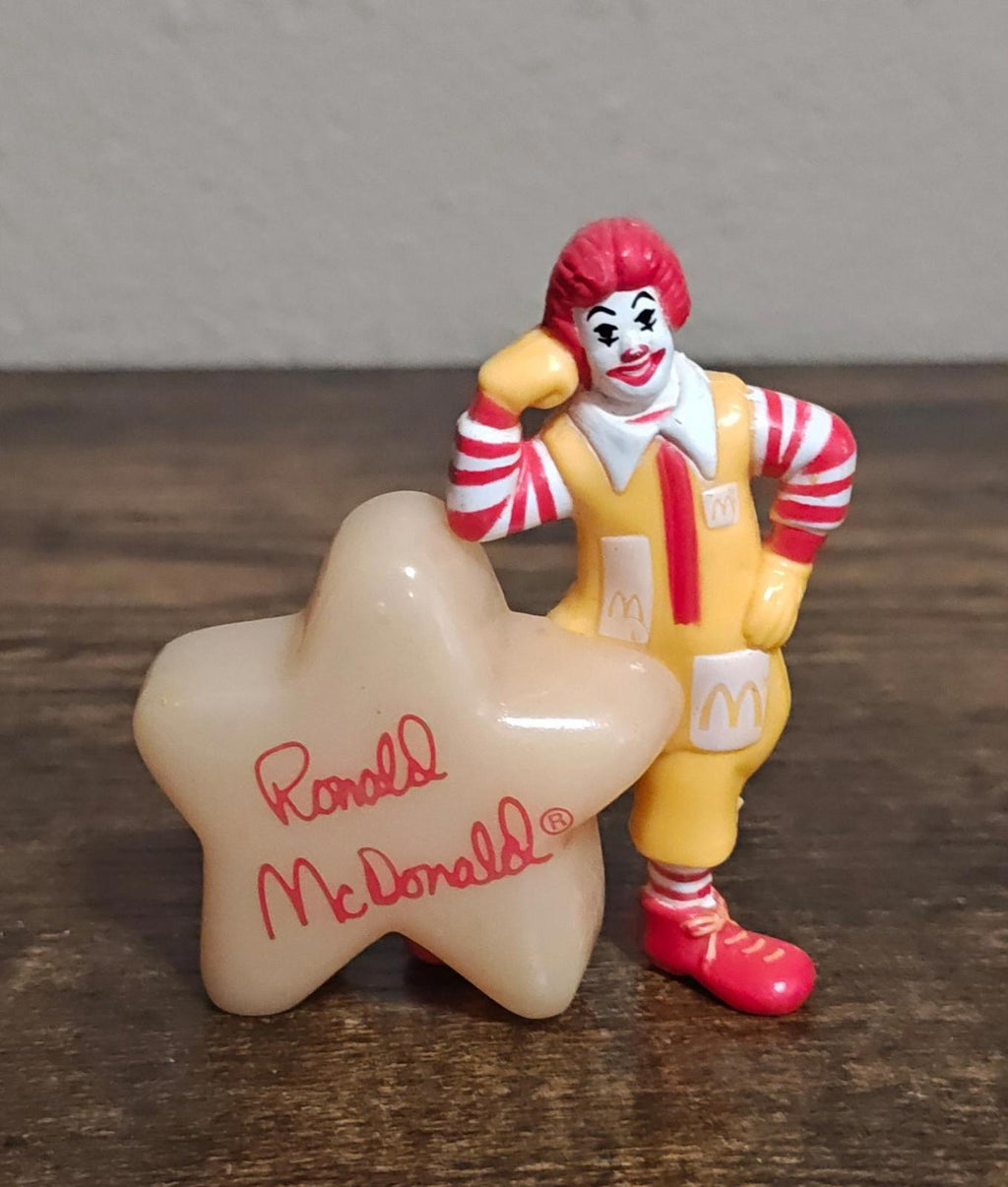 Front view of Ronald McDonald figurine next to a star-shaped glow base with red writing