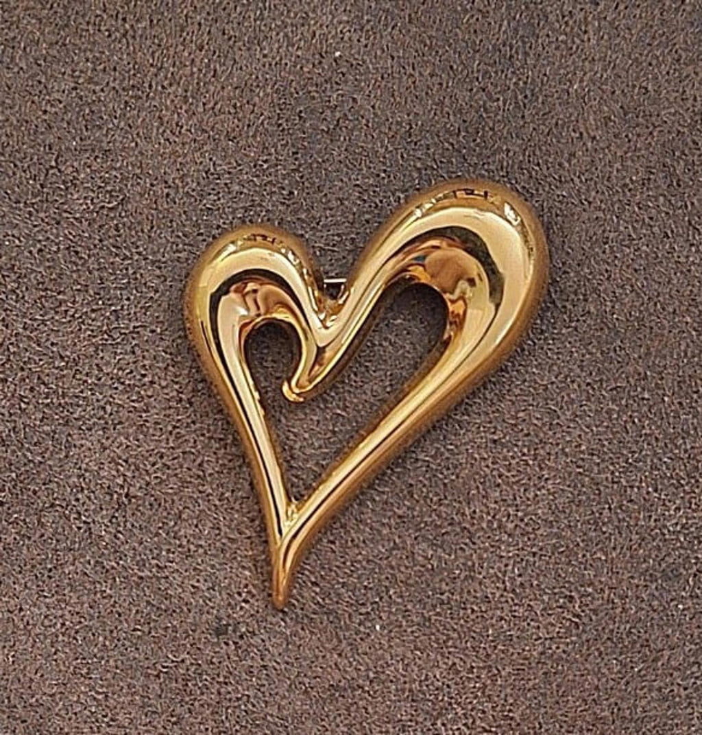 Gold heart pin with open center, polished high-relief border on dark background