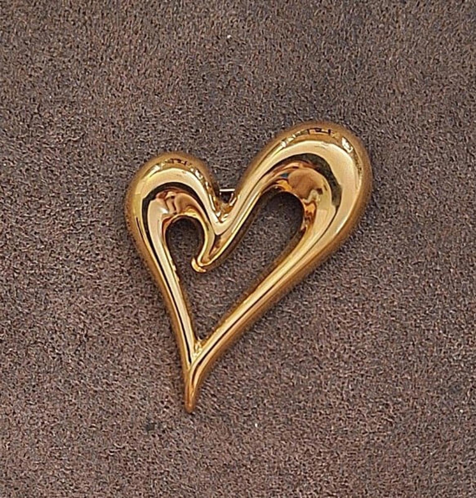 Gold heart pin with open center, polished high-relief border on dark background