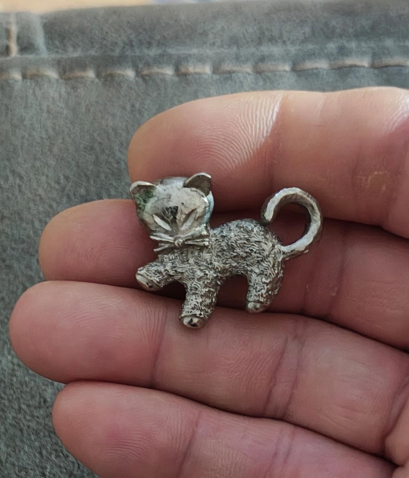 Silver-tone textured cat brooch pin shown from the front on a hand.
