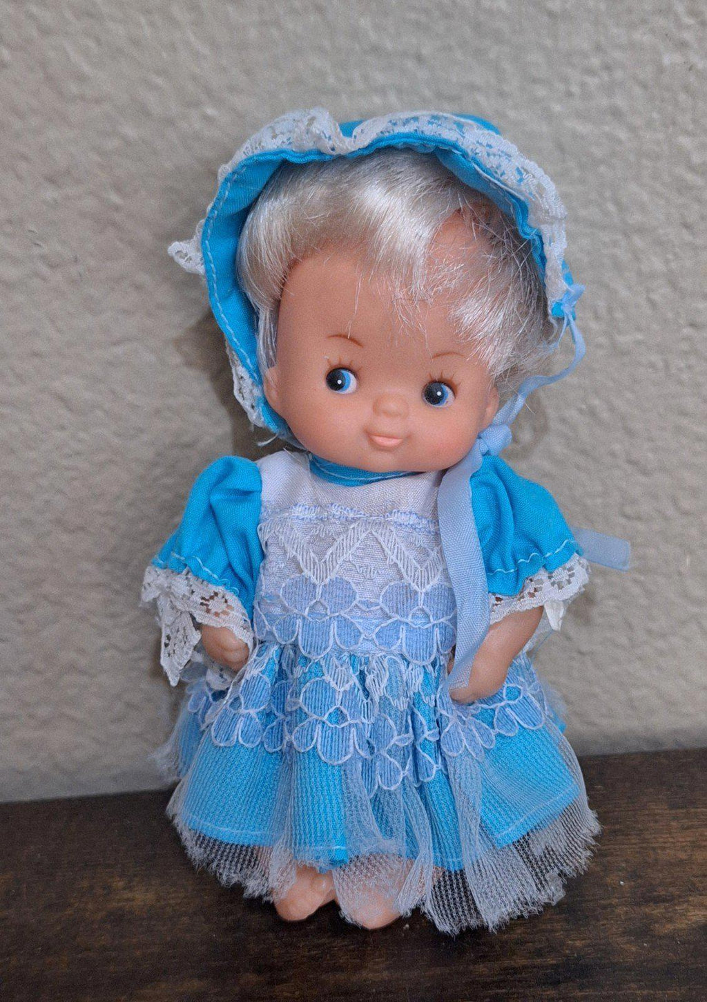Miniature baby doll full-body front in blue bonnet and blue lace dress with blue eyes
