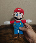 Super Mario plush in blue overalls and red cap, front view held by hand