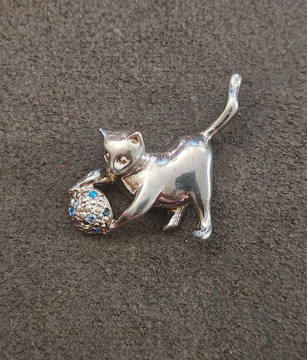 Silver-tone cat brooch holding a ball with blue gem-like stones