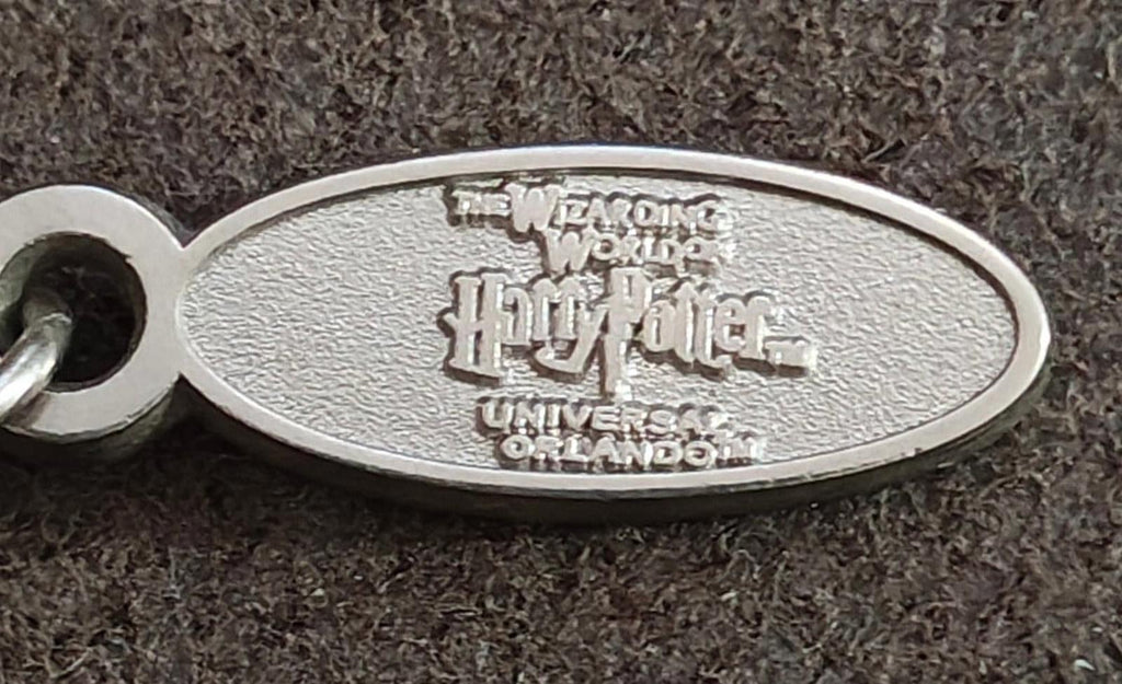 Close-up oval metal charm tag with engraved Wizarding World text