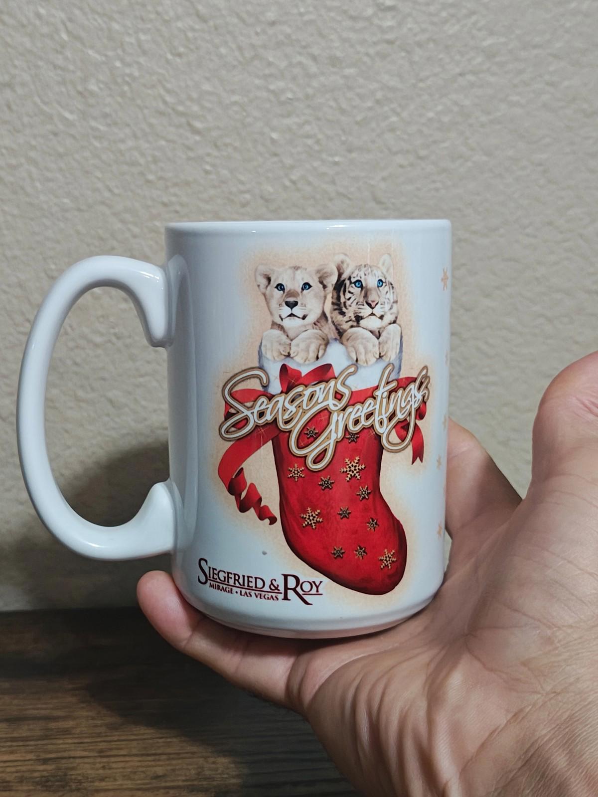 White porcelain mug held in hand, featuring two big cats above a red “Seasons Greetings” stocking