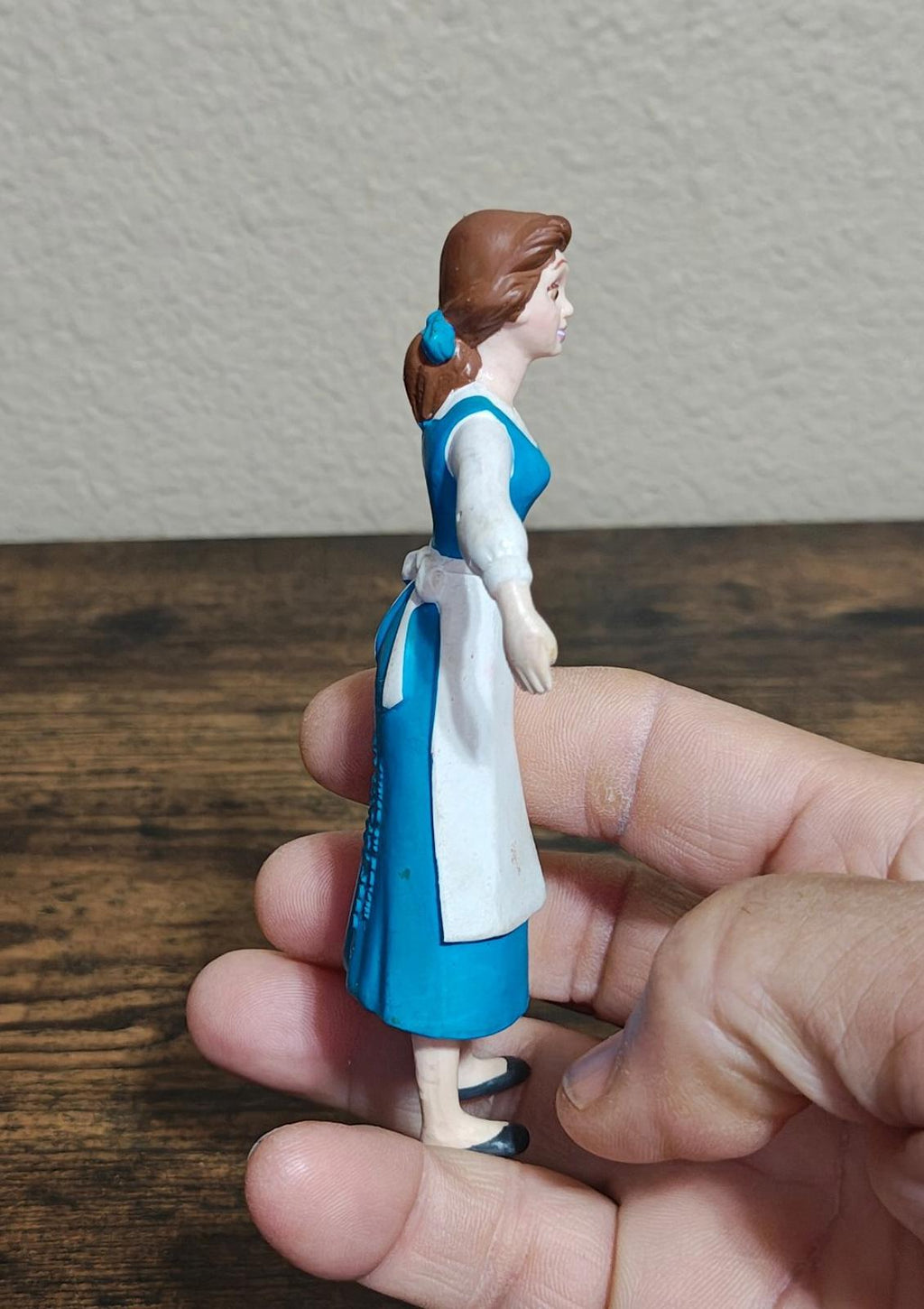 Bendable princess figure side view in blue dress and white apron, brown bun hairstyle