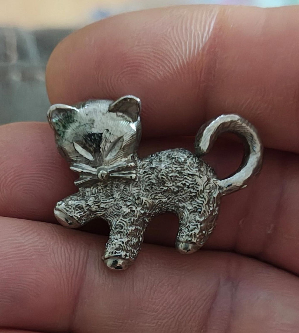 Silver-tone textured cat brooch pin with bow detail and curled tail.