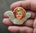 Angel cherub brooch with painted face, light blue wings, and white pearl embellishment