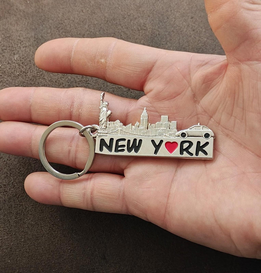 Silver New York keychain held in hand, engraved buildings, red heart "NEW YORK" plate